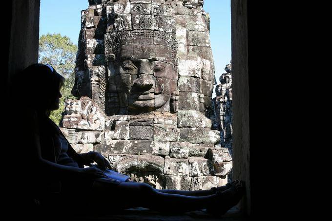 Leyendo a la sombra frente a la cara de piedra, Bayon, Angkor Thom, Angkor, Camboya