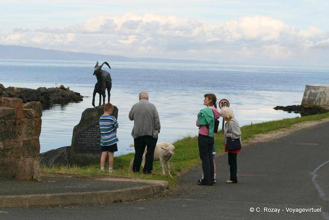 Cabra estatua (cabra), cordero y transeúntes en Cushendun - Irlanda del Norte