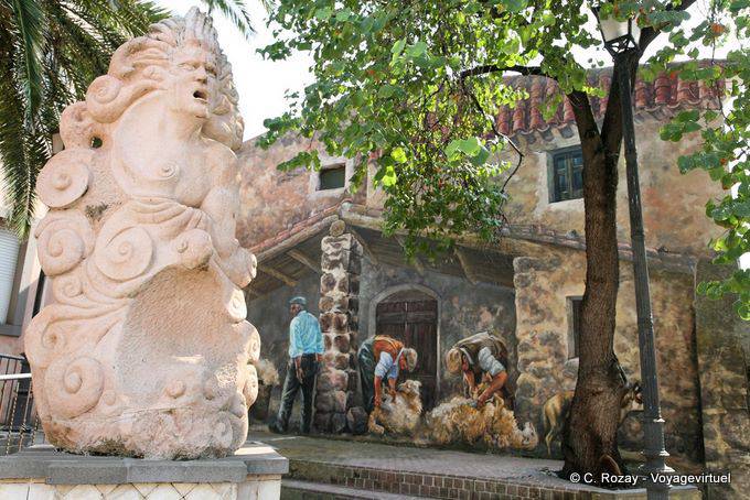 Tinnura, la Piazza del Municipio, la estatua monumental y la pintura de la esquila de ovejas - Cerdena