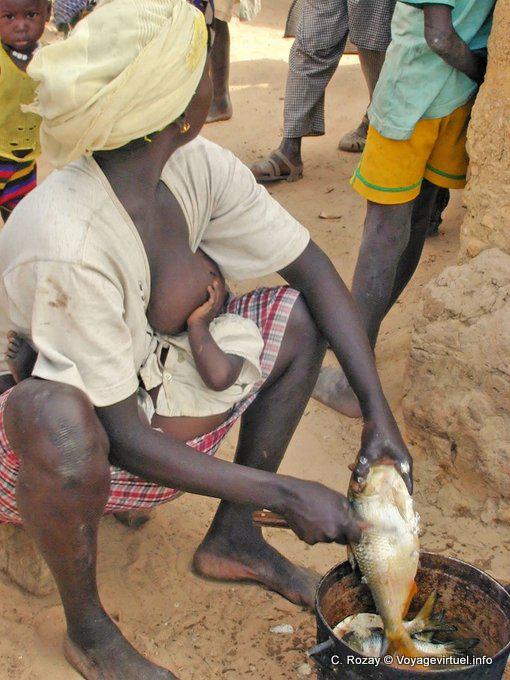 Mujer alimentando a su hijo mientras escamas de pescado - Región Mbam - Senegal